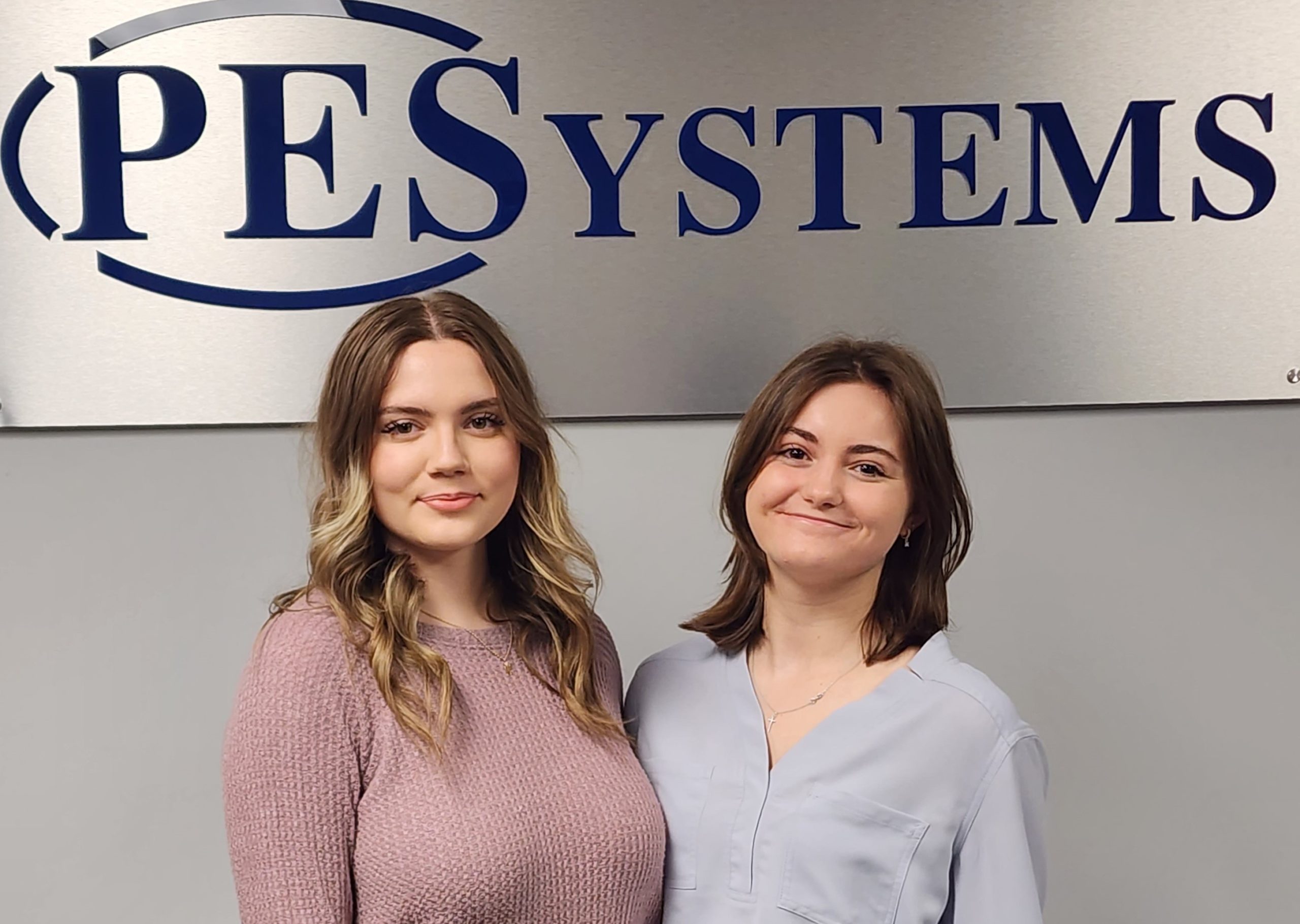 2 girls standing infront of PES logo